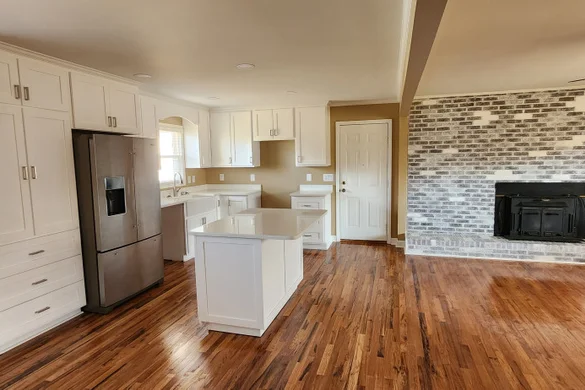 Renovated kitchen with white cabinetry, island, and stone fireplace